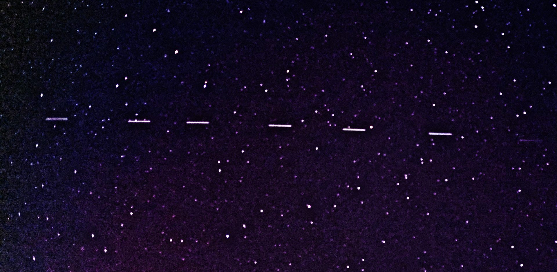A line of newly-launched Starlink satellites, still flying in close single-file formation, photographed against a dark night sky — the same visual phenomenon reported over Vancouver on August 19, 2022